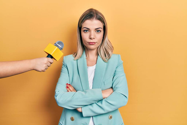 Gyönyörű kaukázusi nőt interjúztat egy riporter, aki szkeptikus és ideges mikrofont tart, és keresztbe tett karokkal helyteleníti az arckifejezését. negatív személy.  - Fotó, kép