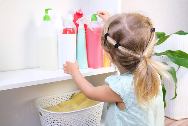 Toddler touches bottles of household chemicals, household cleaning products. Dangerous situation - Foto, afbeelding