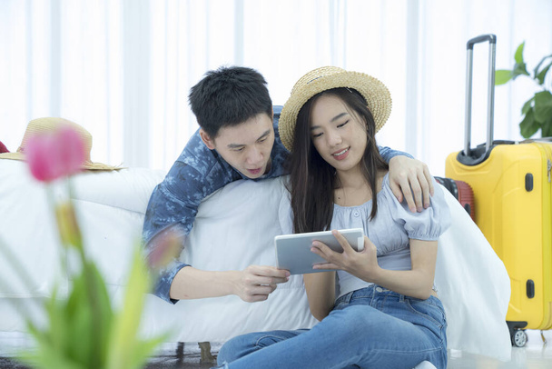 Feliz joven pareja asiática turistas con Tablet PC. Pareja maleta de embalaje en la cama y mintiendo y mirando tableta digital para la búsqueda y planificación de viaje en línea. - Foto, Imagen