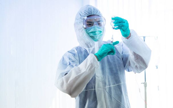 Концепция вакцинации COVID-19. Азиатский врач в медицинской перчатке, маске и костюме СИЗ держит шприц и корону вирусной вакцины. - Фото, изображение