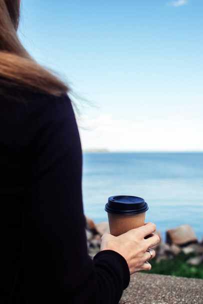 Girl holding coffee on a beautiful background. The concept of the beginning of the morning, vigor and environmental friendliness. Paper cup with takeaway coffee in hand. Vertical photo - Photo, Image