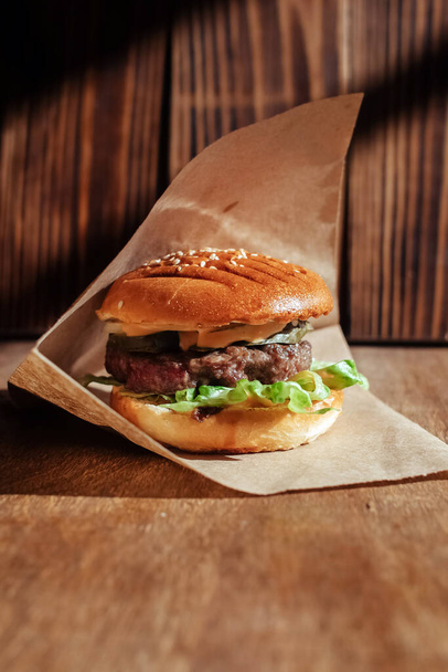 Burger papírcsomagolásban közelkép. Kaja egy gyorsétteremben. Makro fénykép hamburger összetevőkről hússal és zöldséggel - Fotó, kép