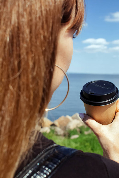 Mädchen mit Kaffee auf einem schönen Hintergrund. Das Konzept des Morgens, Kraft und Umweltfreundlichkeit. Pappbecher mit Kaffee zum Mitnehmen in der Hand. Vertikales Foto - Foto, Bild