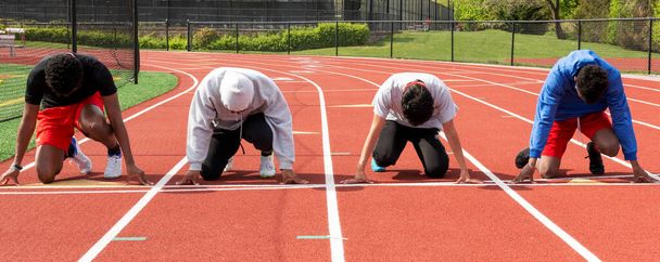 Edessä näkymä neljä lukion pojat sprinters valmiina niiden merkkiin ajaa sprintti rodun toisiaan vastaan harjoituksissa rred radalla. - Valokuva, kuva