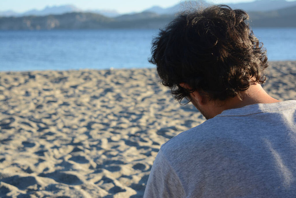 jovem macho com as costas voltadas para a praia olhando para o lago na patagônia argentina calmamente pensando - Foto, Imagem