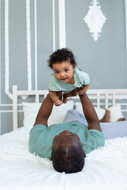 szczęśliwy uśmiech afrykański amerykański tata z małym synem na łóżku w domu przytulanie i zabawy, szczęśliwa rodzina, dzień ojca - Zdjęcie, obraz