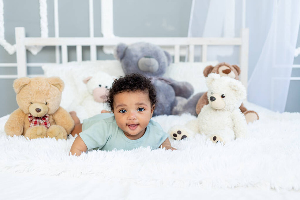 africano americano bebé niño seis meses en cama entre teddy oso juguetes - Foto, imagen