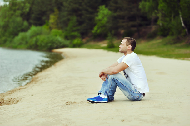 Lonely young man sitting near a lake in a forest - Photo, Image