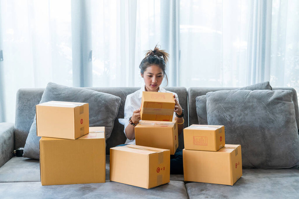 Азиатские женщины, сидящие на диване со множеством коробок с посылками с малым бизнесом, продают клиентам через интернет-магазины. Концепция продажи и покупки онлайн из дома - Фото, изображение