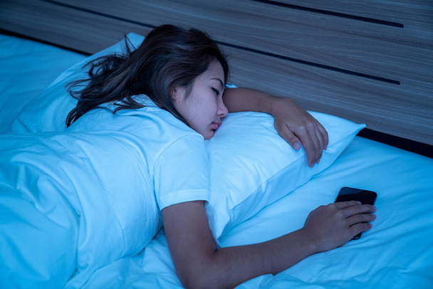 Top View of Beautiful Young Woman Slapen Gezellig op een bed in zijn slaapkamer 's nachts. Ze speelt telefoon tot ze slaapt. - Foto, afbeelding