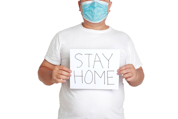 Fat man wearing a mask and white clothes Holding a paper sign, write the words stay home. Concept of health problems for obese people Prevention of coronavirus infection. White background. isolated - Fotoğraf, Görsel