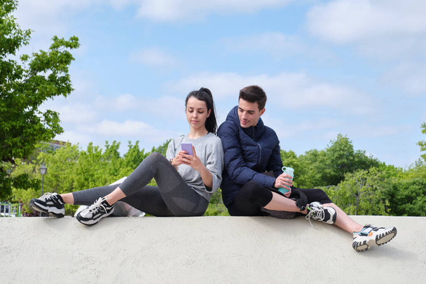 Young sport couple checking at the smartphone while sitting at a park. Fitness technology concept. - Foto, immagini