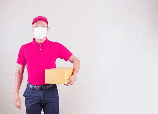asiatico consegna uomo in rosso cap e t-shirt uniforme con maschera viso tenere vuoto scatola di cartone servizio quarantena pandemia coronavirus virus covid concetto. Consegna a domicilio - Foto, immagini