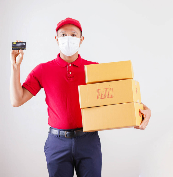 asiatico consegna uomo in rosso cap e t-shirt uniforme con maschera viso tenere vuoto scatola di cartone servizio quarantena pandemia coronavirus virus covid concetto. Consegna a domicilio - Foto, immagini