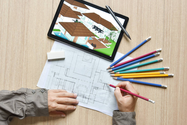 планшет с архитектурным рисунком с детальной перспективой строительства и черновиком плана с цифровыми ручками на деревянном столе, концепция новой технологии работы планшета с цифровой ручкой - Фото, изображение