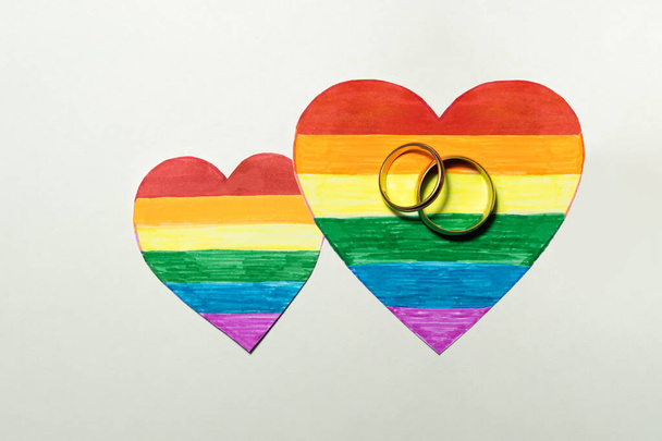 two golden rings as a wedding symbol on the rainbow-colored LGBTQ+ hearts. Love, human rights, tolerance for LGBT people - Photo, Image