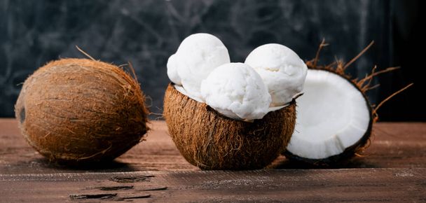 Fresh sweet coconut ice cream in a coconut shell on a wooden table. Sweet summer food.Wide banner. - 写真・画像