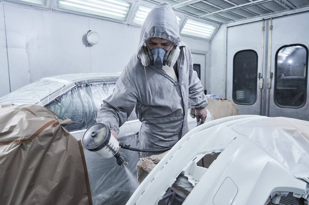 Car painting and automobile repair service. Auto mechanic in white overalls paints car with airbrush pulverizer in paint chambe - Foto, immagini
