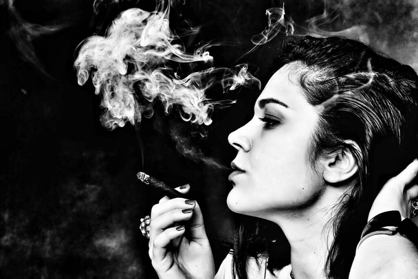 Schöne europäische bossy brünettes Mädchen raucht einen Zigarillo wie ein Chef im Studio auf isoliertem Hintergrund. Modeln, Stil, Modekonzept. Noir-Effekt - Foto, Bild