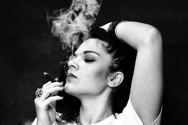美しいヨーロッパの巨乳ブルネットの女の子は、孤立した背景でスタジオのボスのようにタバコを吸っています。モデリング、スタイル、ファッションコンセプト。ノワール効果 - 写真・画像
