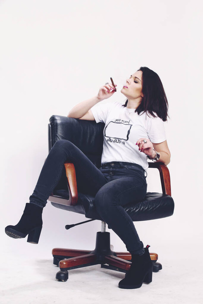 Mooi europees bazig brunette meisje rookt een sigarillo als een baas in de studio op geïsoleerde achtergrond. Modellenwerk, stijl, mode concept. Noir effect - Foto, afbeelding