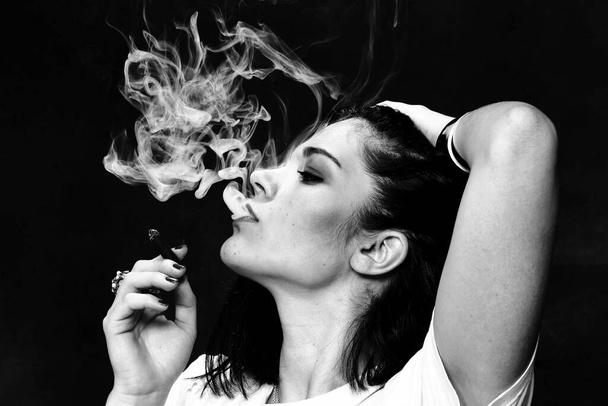 Beautiful european bossy brunette girl smoking a cigarillo like a boss in studio on isolated background. Modeling, style, fashion concept. Noir effect - Photo, Image