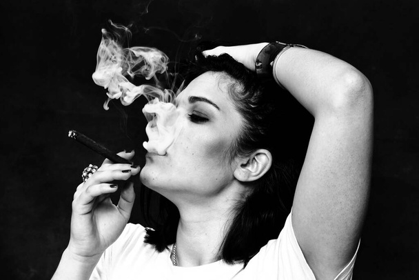 Belle fille brune autoritaire européenne fumant un cigarillo comme un patron en studio sur fond isolé. Modélisation, style, concept de mode. Effet noir - Photo, image