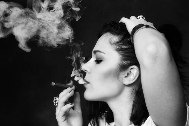 Beautiful european bossy brunette girl smoking a cigarillo like a boss in studio on isolated background. Modeling, style, fashion concept. Noir effect - Φωτογραφία, εικόνα