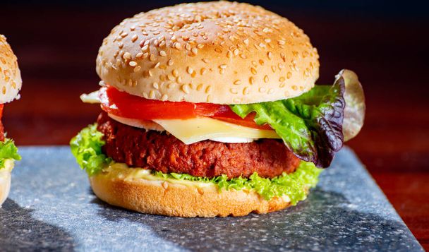 Comida vegetariana saborosa, cheeseburgers caseiros feitos de carne de soja à base de plantas com queijo, cebola, alface verde e tomate de perto - Foto, Imagem