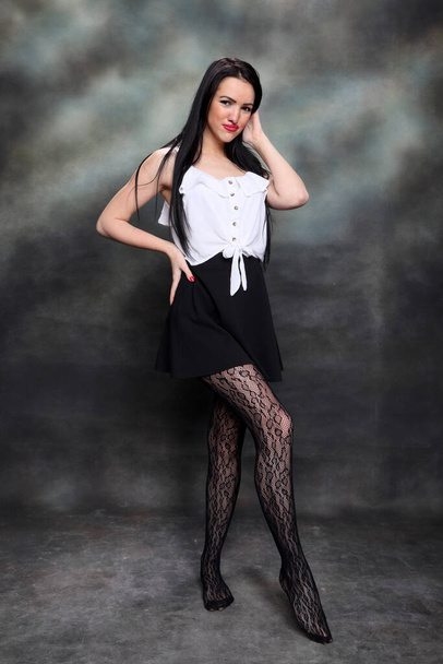Schöne europäische Mädchen mit langen schwarzen Haaren posiert im Studio auf Leinwand Hintergrund. Stil, Trends, Modekonzept. - Foto, Bild