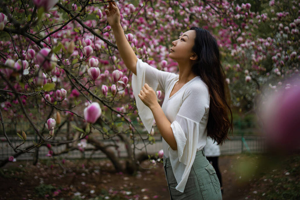 Houkutteleva aasialainen nainen kevätpuutarhassa Magnolian kanssa. Kevään tausta. Naistenpäivä - Valokuva, kuva