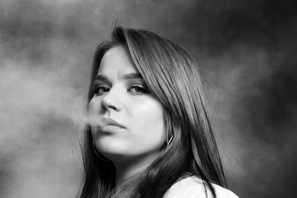 Aantrekkelijk brunette meisje poseert in de studio en rookt een sigaar. Noir, retro stijl fotografie. Glamour, lifestyle, modeconcept. - Foto, afbeelding