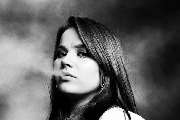 Attractive brunette girl posing in studio and smoking a cigar. Noir, retro style photography. Glamour, lifestyle, fashion concept. - Photo, Image