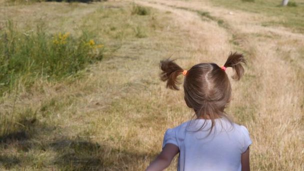 Toddler girl back running bu countryside road. Child with blonde ponytails jumping - Photo, Image