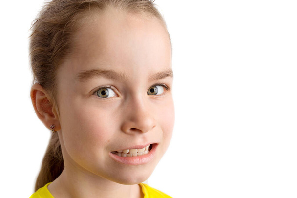 Klein meisje staat op een witte achtergrond met een mooie glimlach, kinderen scheef gebit, pediatrische tandheelkunde. Scheve tanden van dichtbij. Correctie van malocclusie is vereist. - Foto, afbeelding