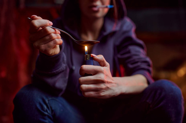 Drug addict woman with spoon and fire prepares dose, shebang interior on background, den. Narcotic addiction problem, eternal depression - Foto, Imagen