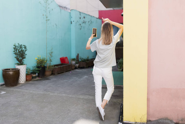 Pretty laughing caucasian woman with smartphone has good time outdoor. portrait of trendy millennial girl with blonde hair wears fashionable clothing - 写真・画像