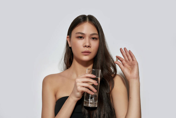 Jovem menina asiática segurando pílula e vidro de água - Foto, Imagem