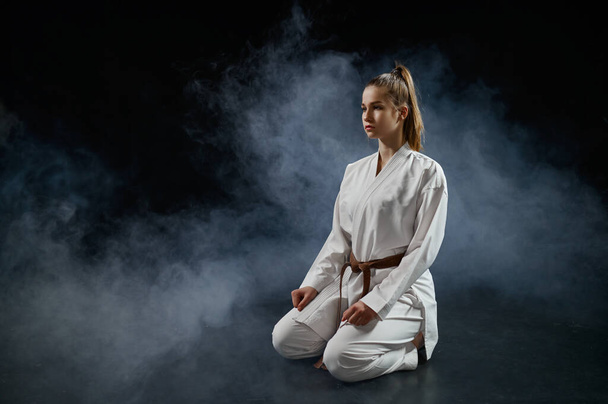 Female karateka on training in white kimono sitting on the floor, dark background. Karate fighters on workout, martial arts, women fighting competition - Foto, Bild
