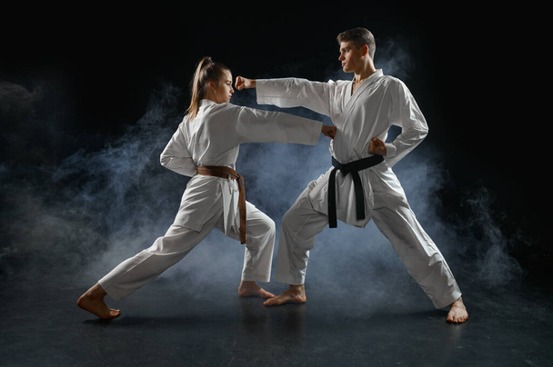 Combattant de karaté féminin à l'entraînement avec maître, kimono blanc, fond sombre fumé. Karateka sur l'entraînement, les arts martiaux, la compétition de combat - Photo, image