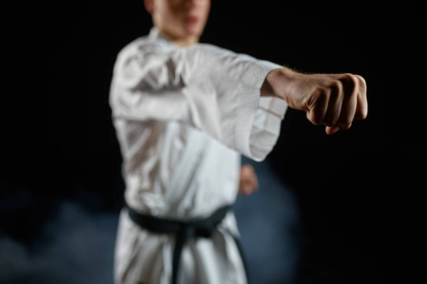 Αρσενικό καρατέκα, εξάσκηση στο λευκό κιμονό, στάση μάχης, σκούρο φόντο. Man on karate workout, πολεμικές τέχνες, εκπαίδευση πριν από την καταπολέμηση του ανταγωνισμού - Φωτογραφία, εικόνα