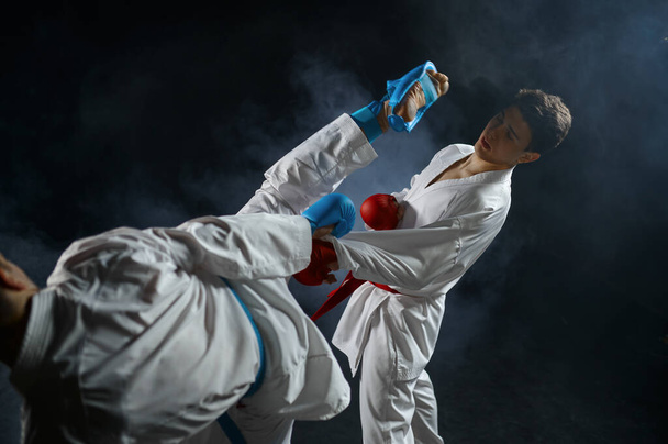 Dva karatekové v bílém kimonu a rukavicích, boj v akci, tmavé pozadí. Bojovníci na cvičení, bojová umění, bojová soutěž - Fotografie, Obrázek