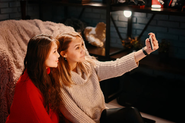 Two beautiful girls in knitted sweaters take selfies. - Fotoğraf, Görsel