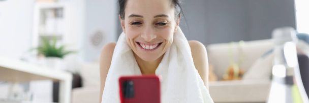 Femme en vêtements de sport couché sur tapis de gymnastique et regardant sur l'écran du téléphone - Photo, image
