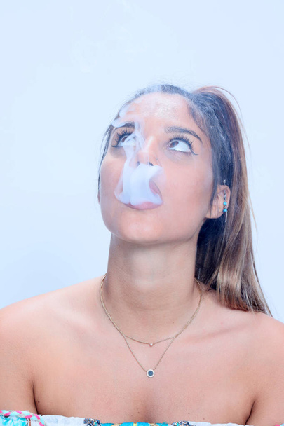 Linda modelo feminina morena posando em estúdio e fumando um charuto elétrico em fundo isolado. Estilo, tabagismo, conceito de moda. - Foto, Imagem
