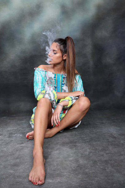 Krásná brunetka ženský model pózuje ve studiu a kouření elektrický doutník na izolovaném pozadí. Styl, kouření, módní koncept. - Fotografie, Obrázek