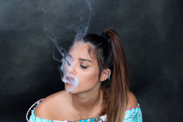 スタジオでポーズをとって孤立した背景で電気シガーを吸う美しいブルネットの女性モデル。スタイル、喫煙、ファッションコンセプト. - 写真・画像