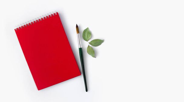 Rood notitieblok met een penseel op een witte achtergrond. Bovenaanzicht, indeling. - Foto, afbeelding