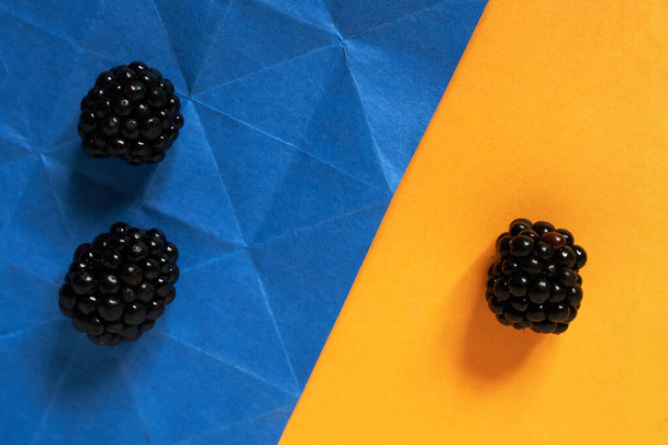 Three blackberries on a blue and yellow paper background, one vs two - Photo, Image