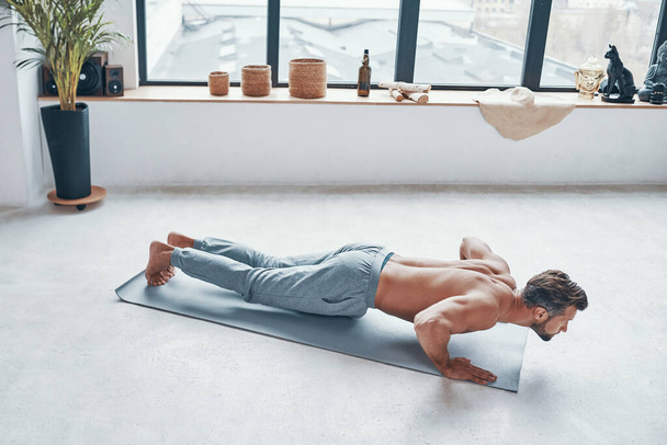Handsome young man keeping plank position while exercising at home - Fotó, kép